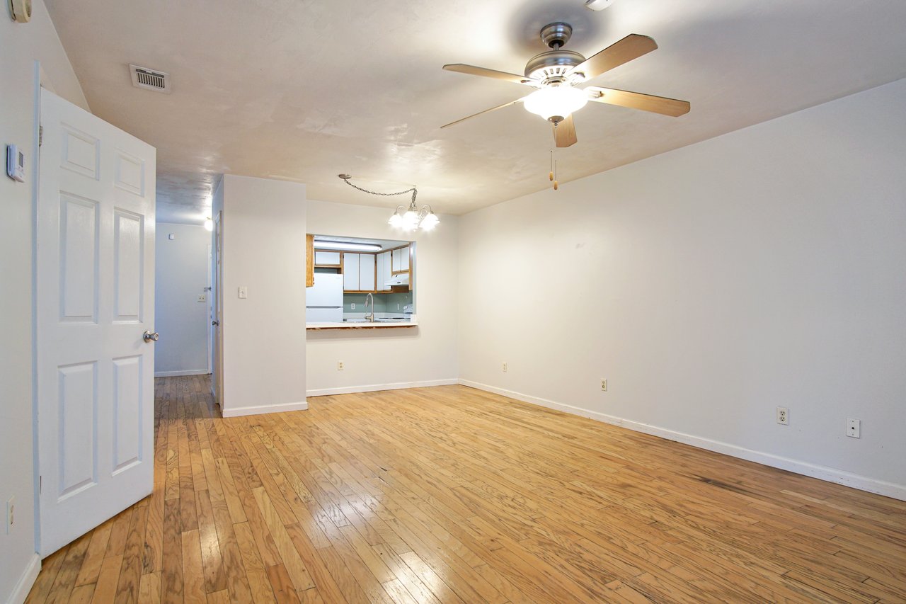 An empty room featuring hardwood floors and a ceiling fan, creating a spacious and airy atmosphere.