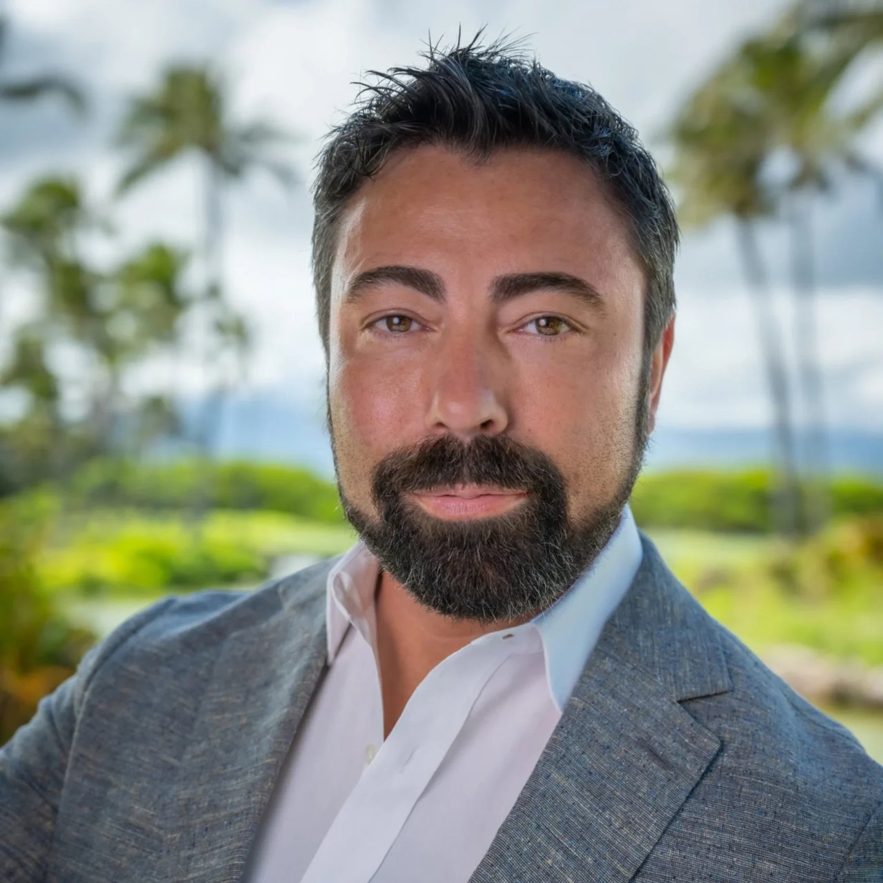 Chris Stiebler in a gray blazer, with palm trees and greenery in the background.