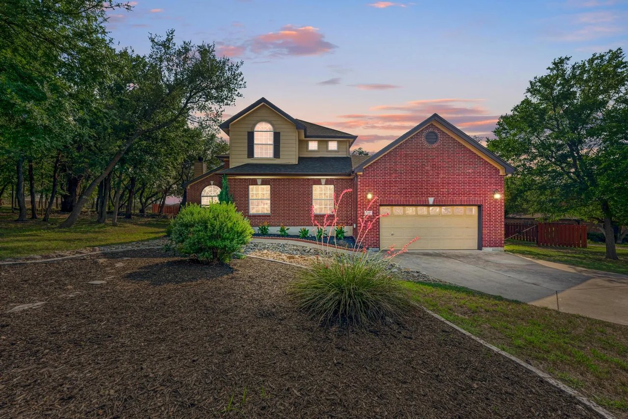 Two-story red-brick home with an attached garage, landscaped yard, and mature trees at dusk.