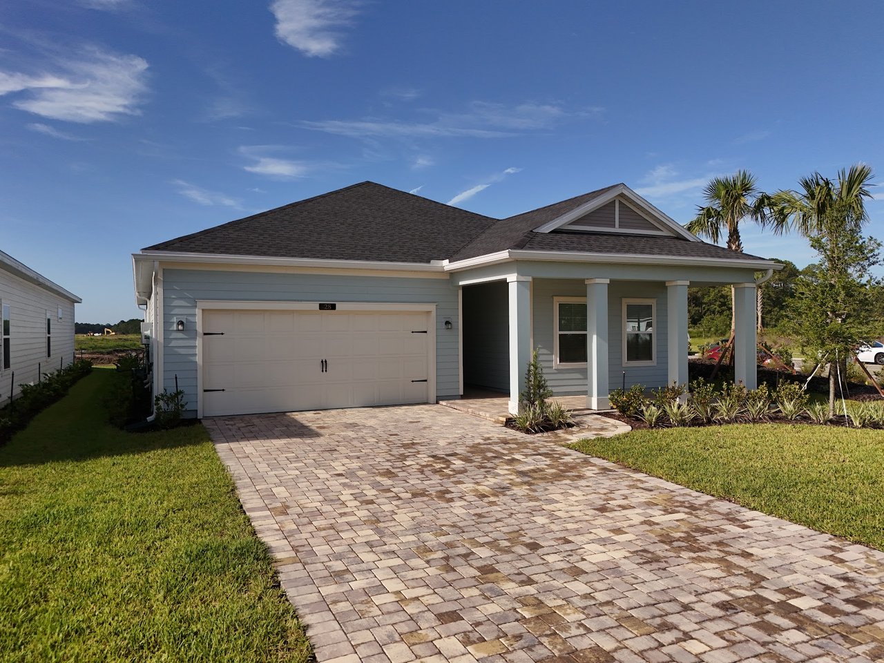 Blue-gray single-story home with a two-car garage, covered porch, and wide paver driveway.
