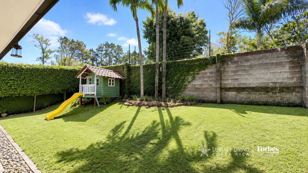 Landscaped backyard with a green playhouse and yellow slide on a sunny lawn.