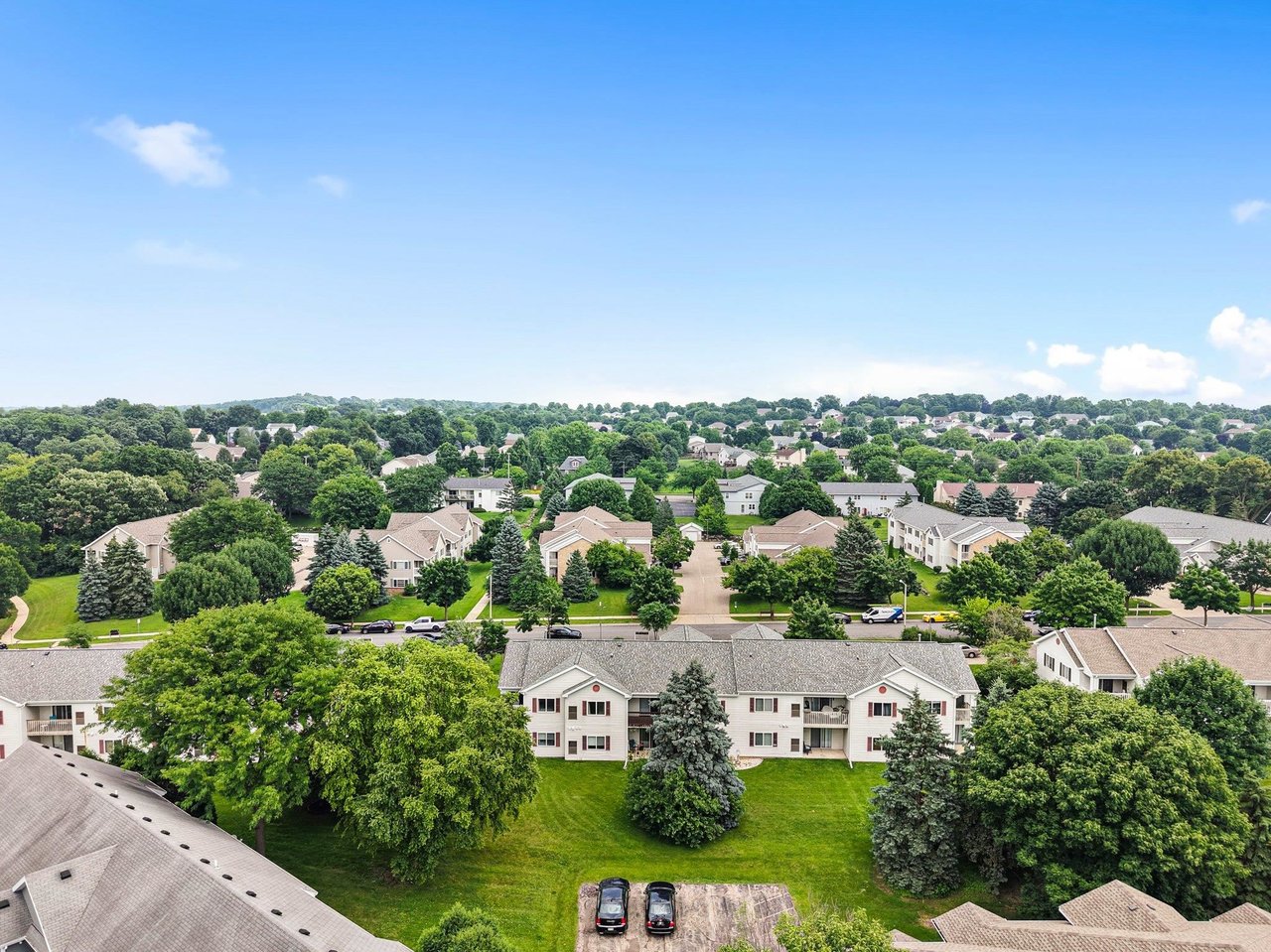Aerial view of residential buildings, neighborhood streets, and mature trees beneath a blue sky.