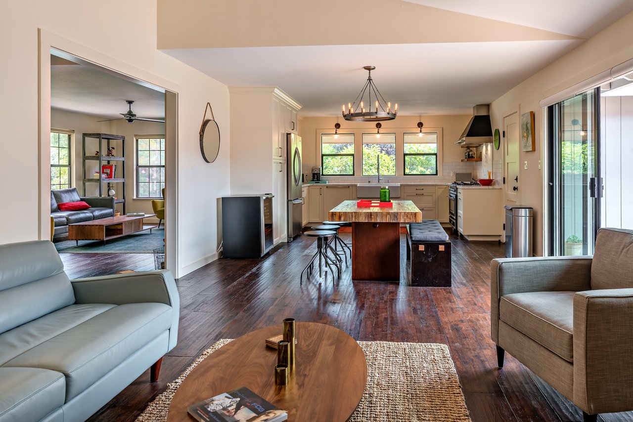 Open-plan kitchen and living room with a wood-topped island, dark hardwood floors, and sliding glass doors.