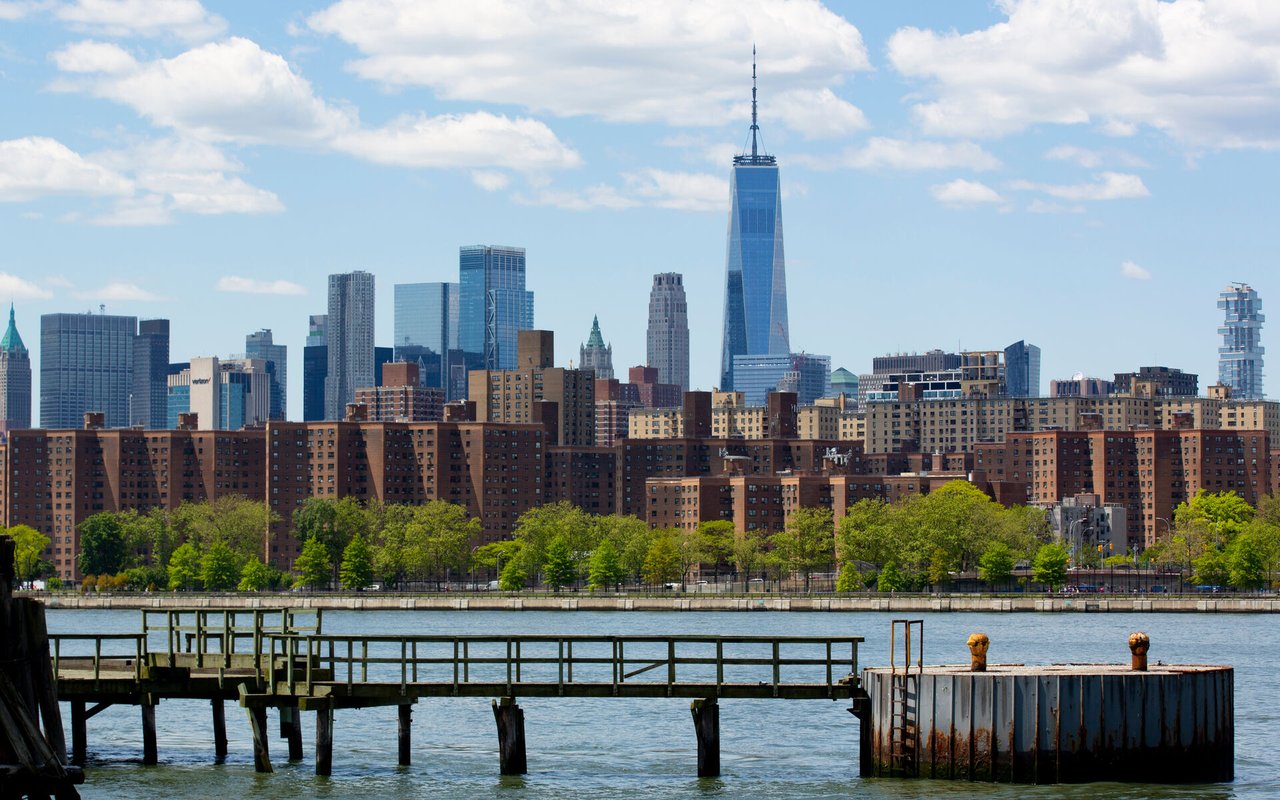 Lower Manhattan skyline with One World Trade Center across the river, viewed from a waterfront pier.