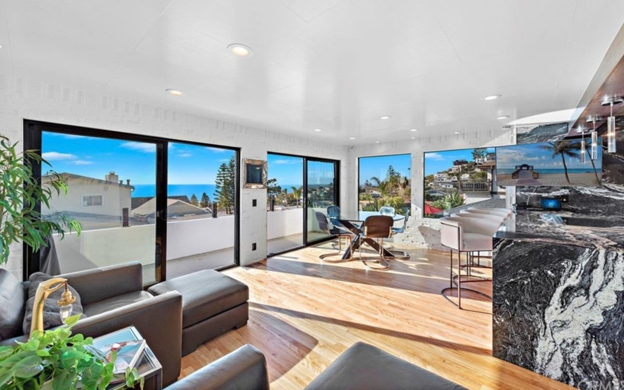 Modern living room with wood floors, marble island, and ocean views through broad windows.