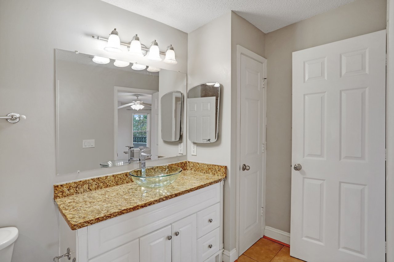 Bathroom with a glass vessel sink, mottled granite vanity, and multiple mirrors.