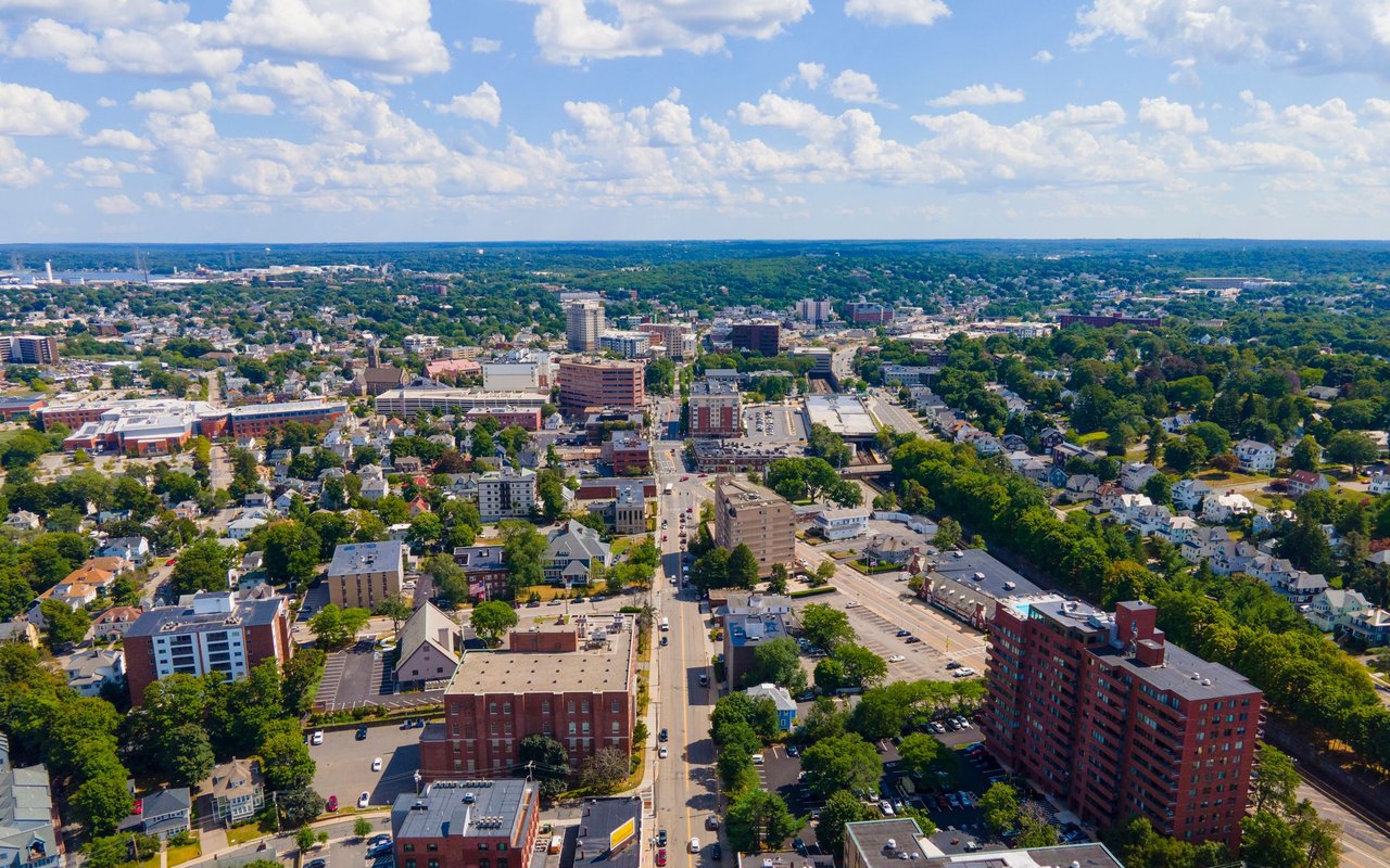 Aerial view of a Massachusetts town center with leafy neighborhoods and a main road.