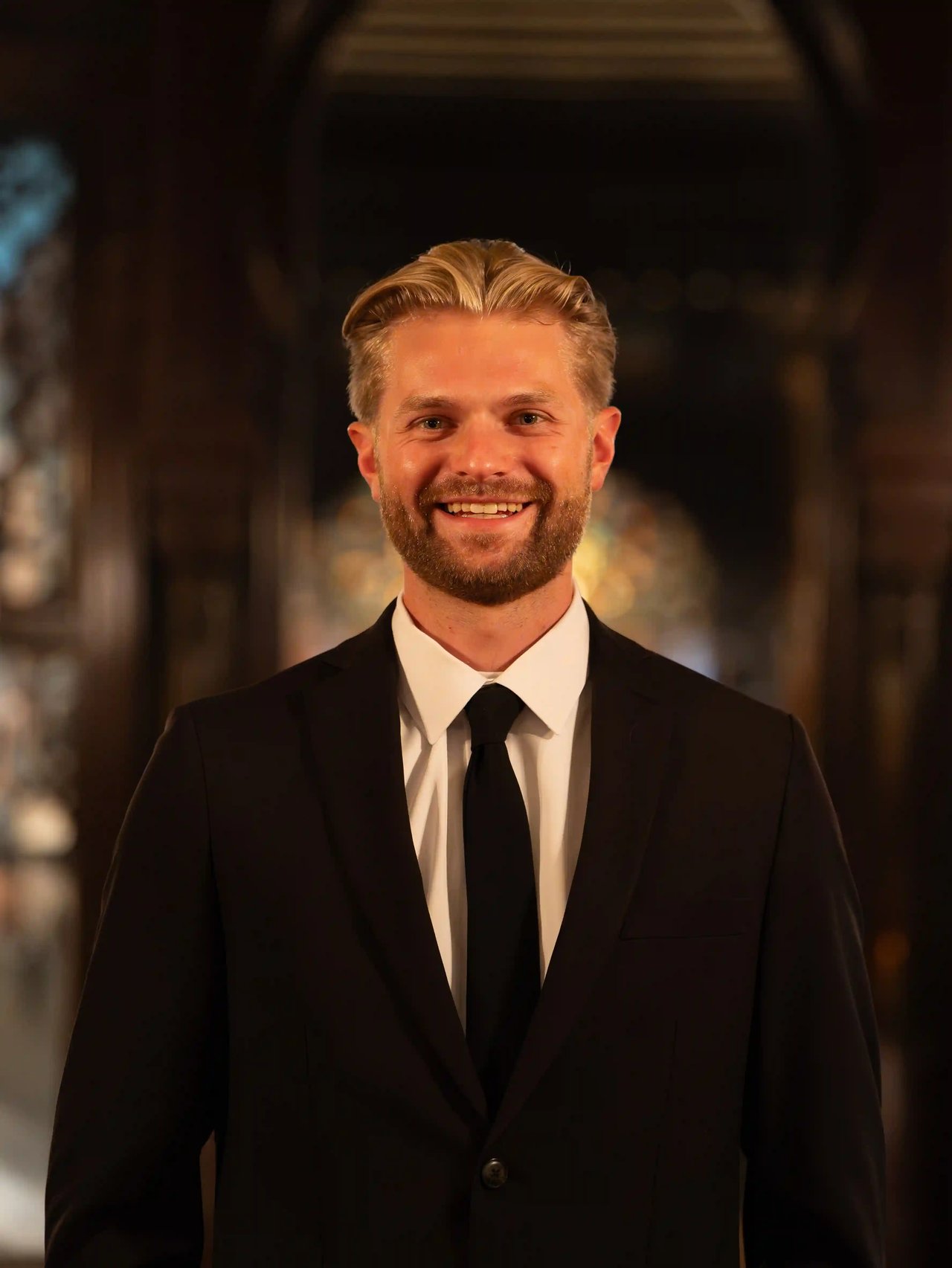 Kyle Ristow, top Milwaukee realtor, smiling in a suit inside an elegant interior setting.