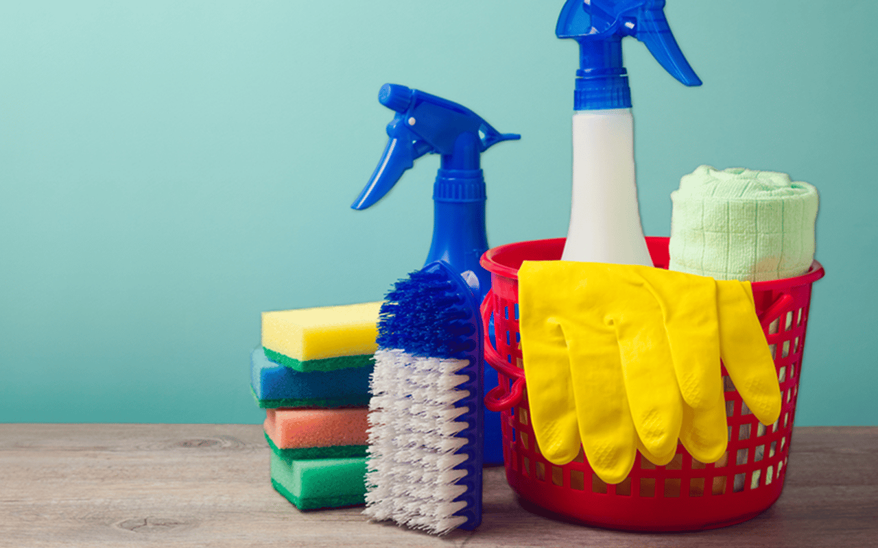 Cleaning supplies in a red basket with yellow gloves, spray bottles, sponges, and a scrub brush.