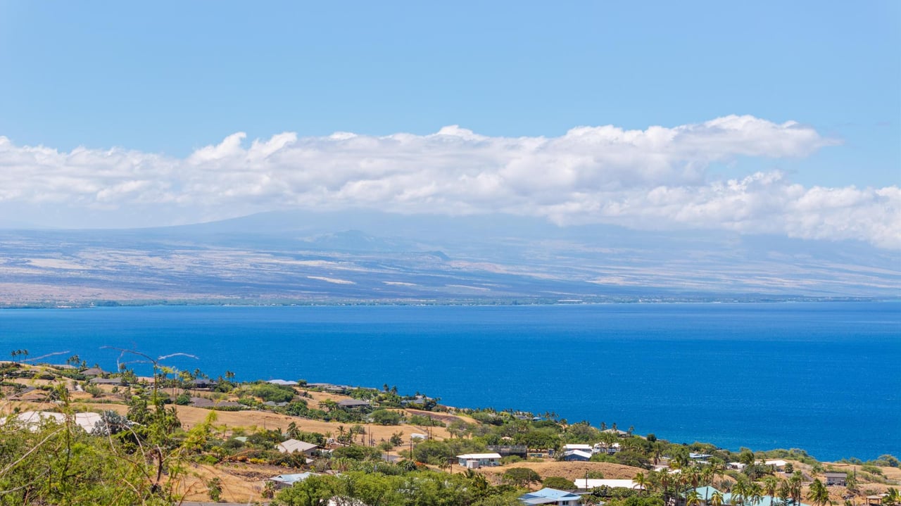 Blue ocean and distant mountains beyond a sunlit Hawaiian coastline.