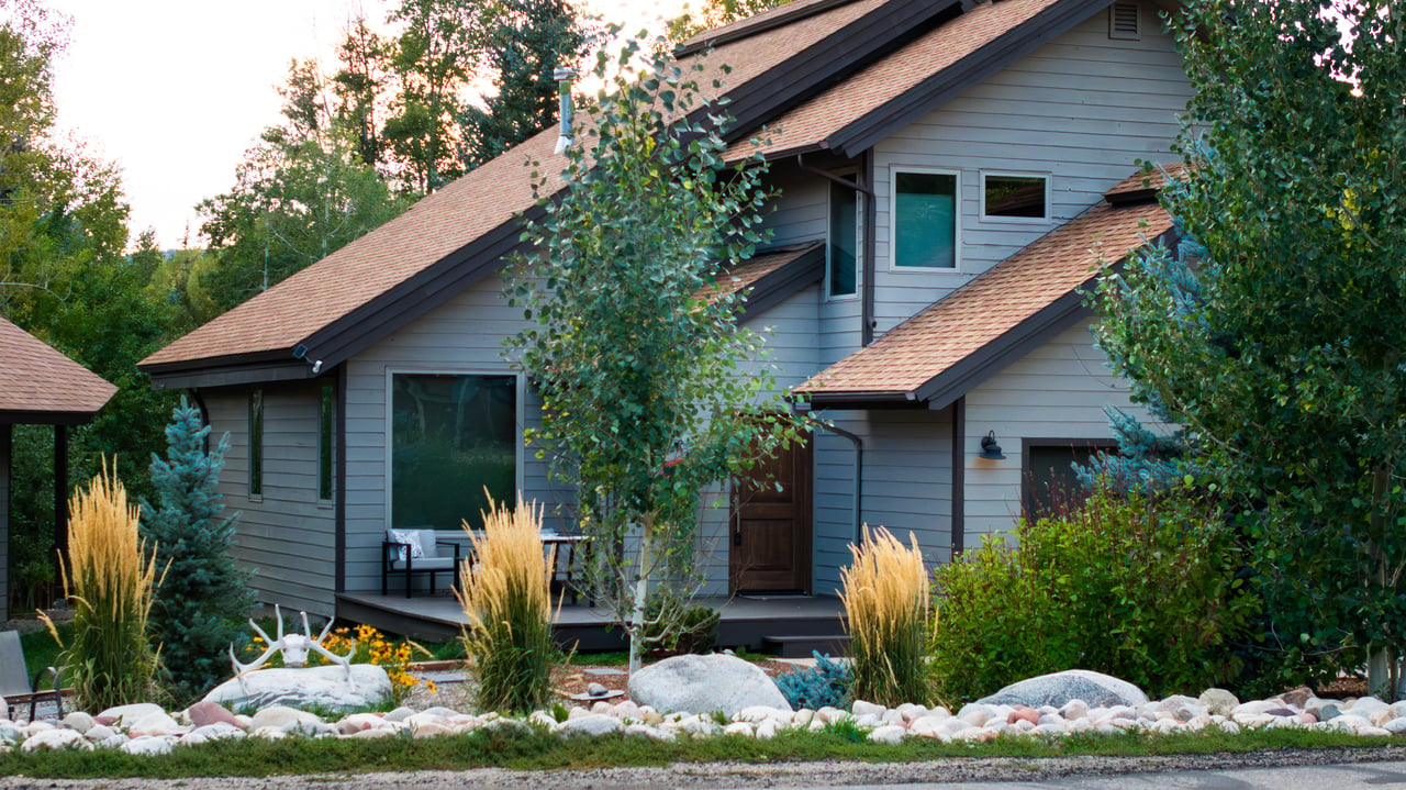 Gray-sided home with multiple gabled roofs, a small patio, and landscaped rock garden.