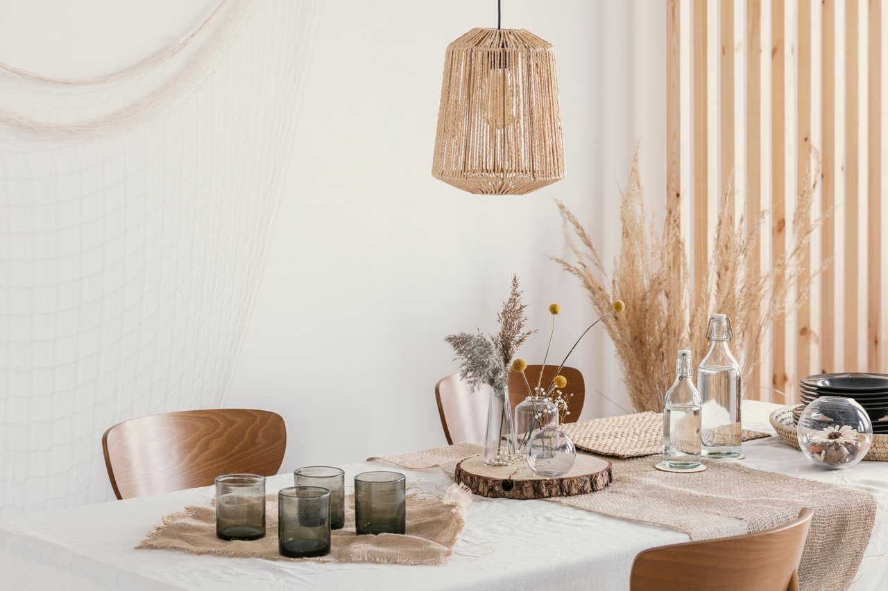 Staged dining room with a woven pendant lamp, neutral table setting, and wooden chairs.