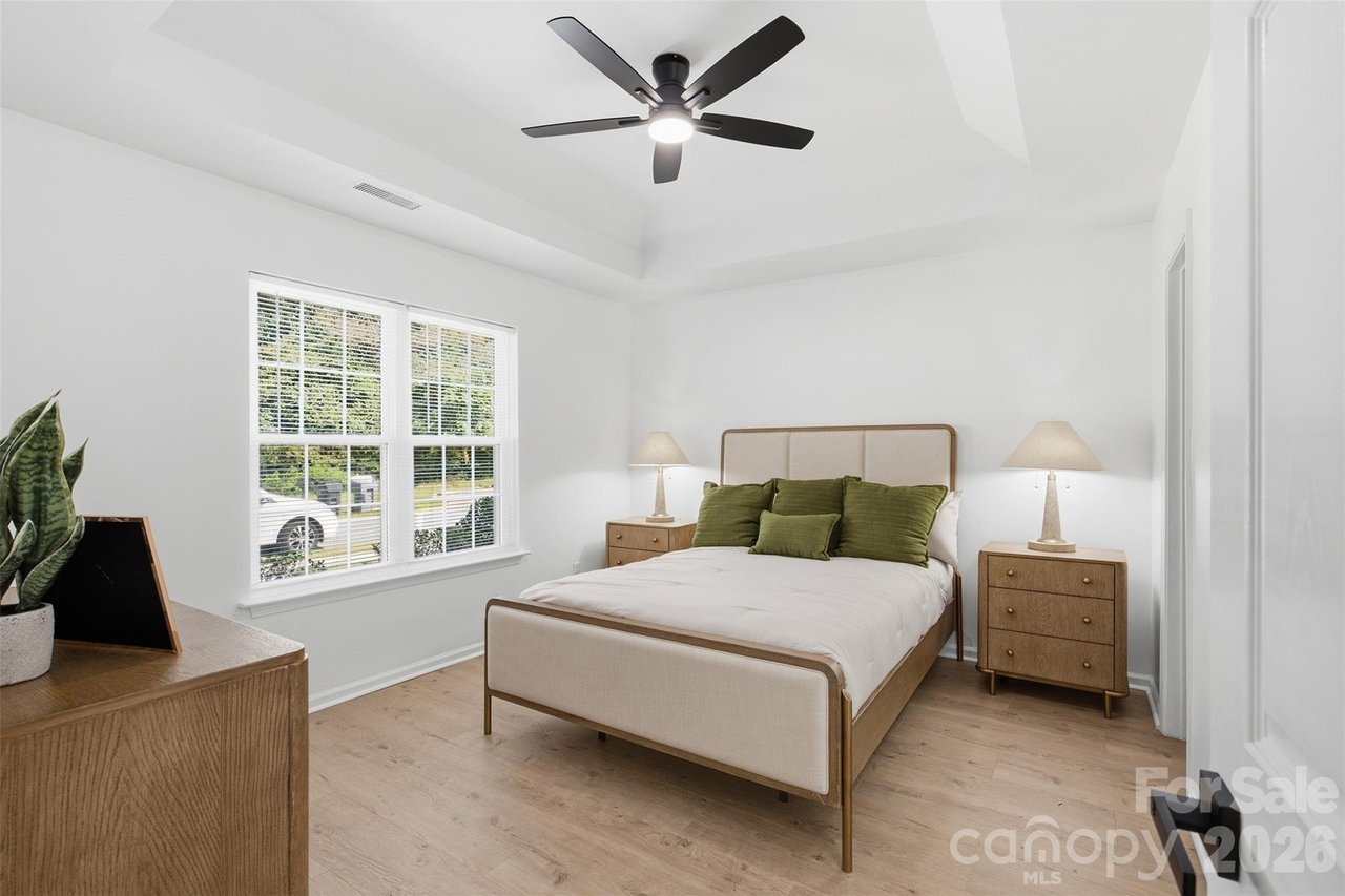 Bedroom with a cream bed, green pillows, matching nightstands, and two windows with white blinds.