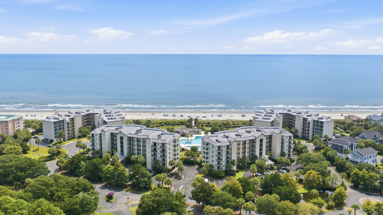 Aerial view of beachfront villas and condominium buildings beside a sandy beach and ocean.