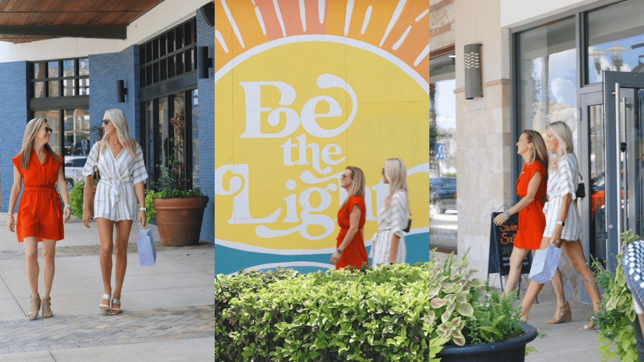 Two women walk through an outdoor shopping center beside a “Be the Light” mural.