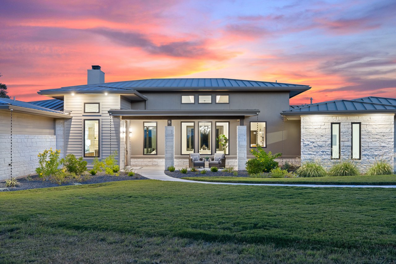 Twilight front elevation of this Hill Country modern home on Caudill Lane in the Bee Caves area of Austin, Texas, with metal roof accents and a stone and siding exterior.