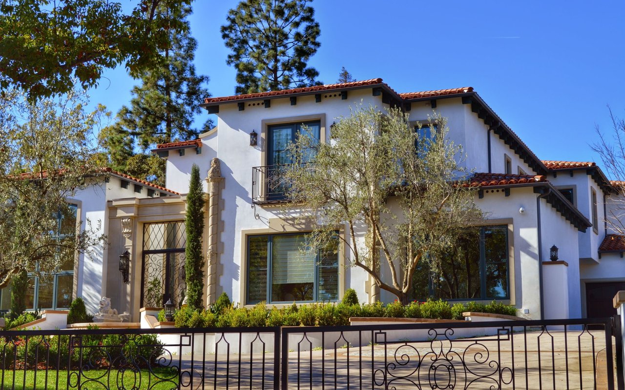 Two-story stucco home with a red tile roof, landscaped yard, and ornate wrought-iron gate.