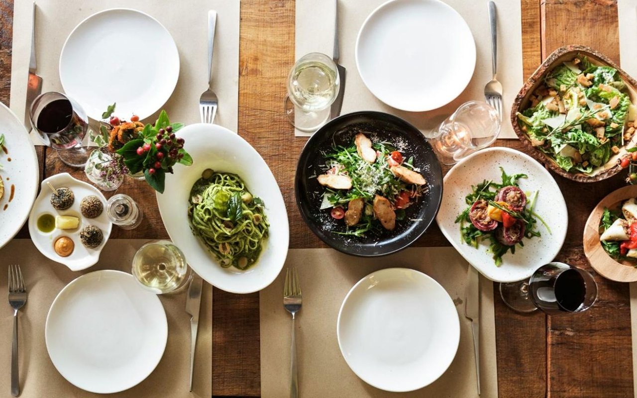 A table set with pasta, salad, appetizers, and wine glasses.