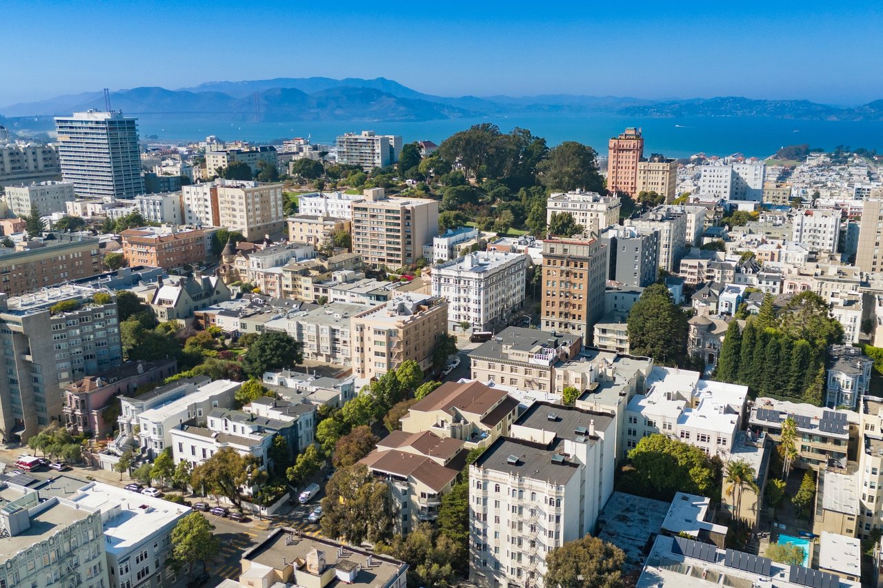 Aerial view of San Francisco buildings with the bay and distant hills in the background.
