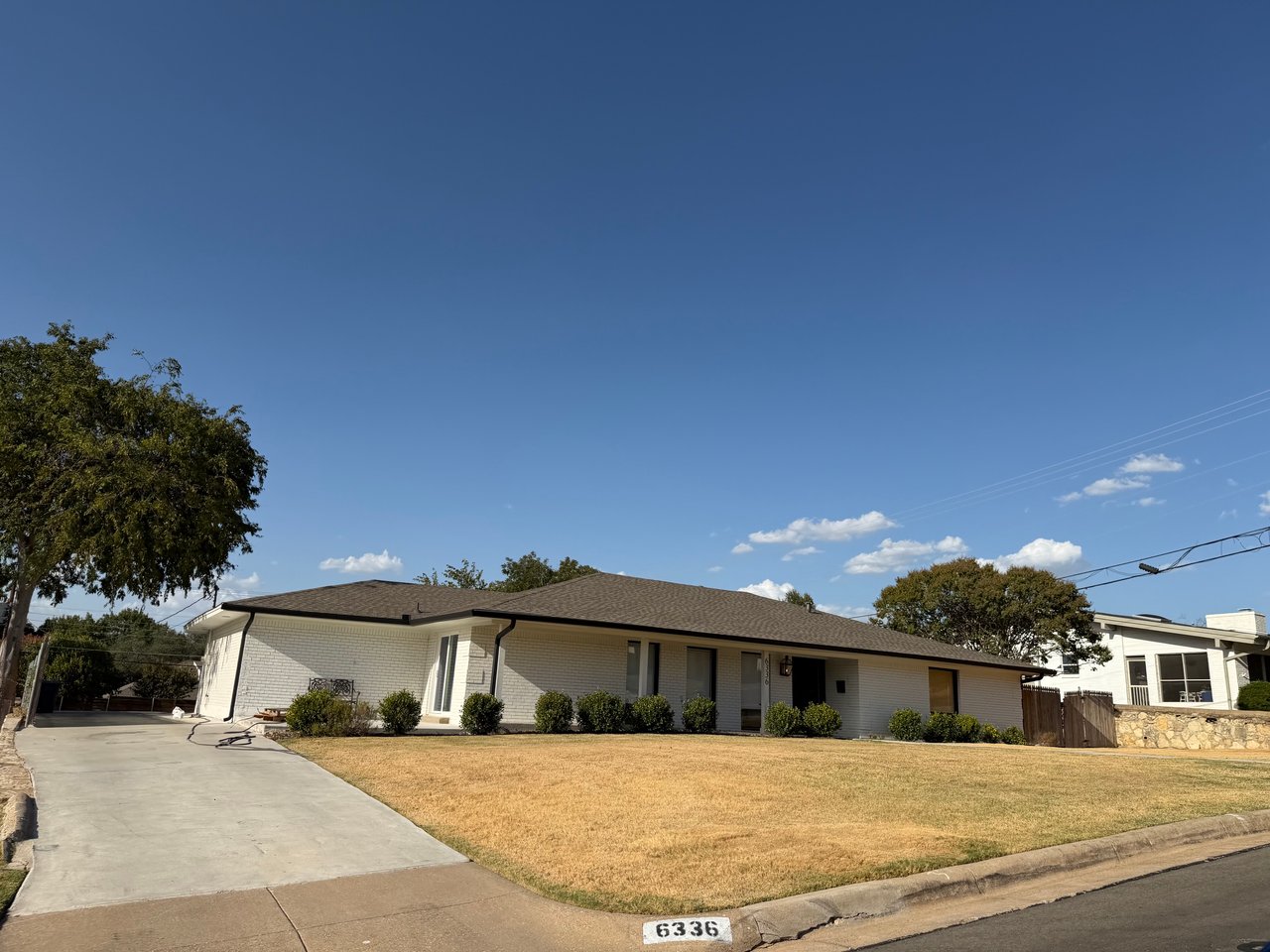Single-story white brick ranch with a broad brown roof, concrete driveway, and dry front lawn.