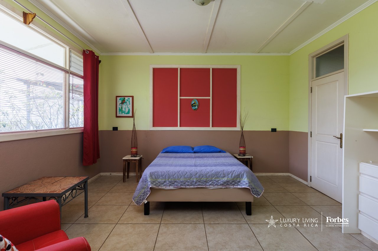 Bedroom with a double bed, blue bedding, red wall panels, and a large window with blinds.