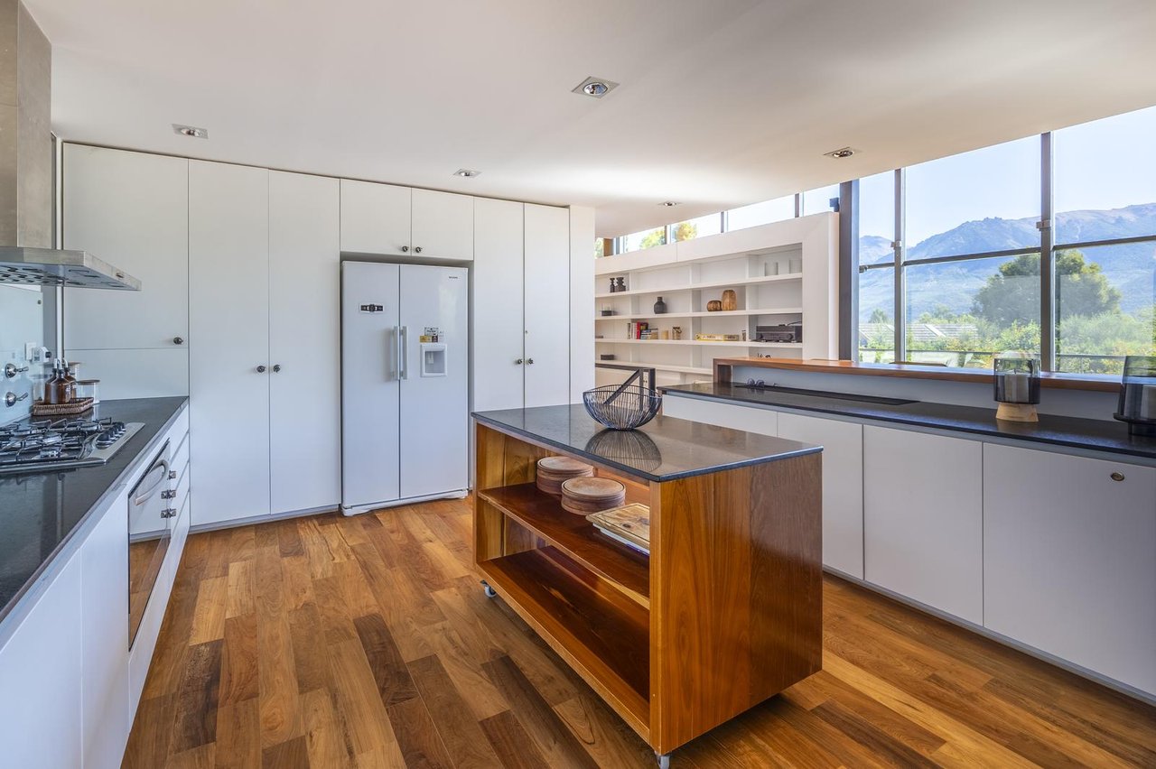 Modern white kitchen with a wooden island and mountain views through wide windows.