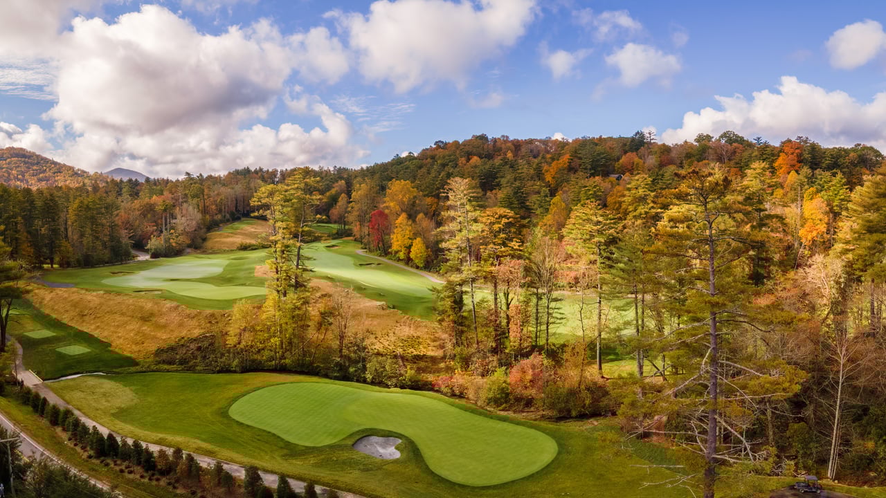 A scenic golf course in highlands, north carolina a hidden gem for real estate agents, is surrounded by vibrant autumn trees under a partly cloudy sky.
