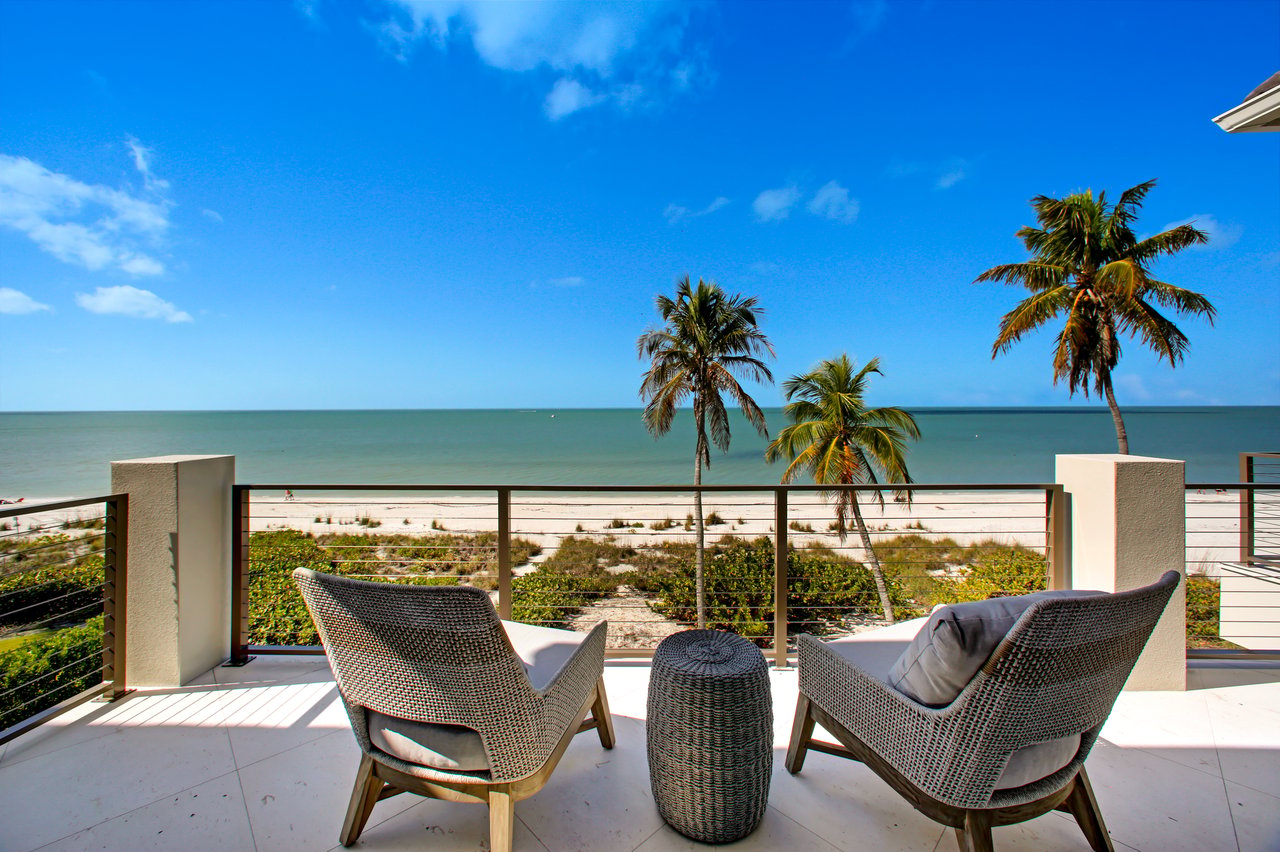 Seaside terrace with wicker chairs overlooking a sandy beach and calm ocean.