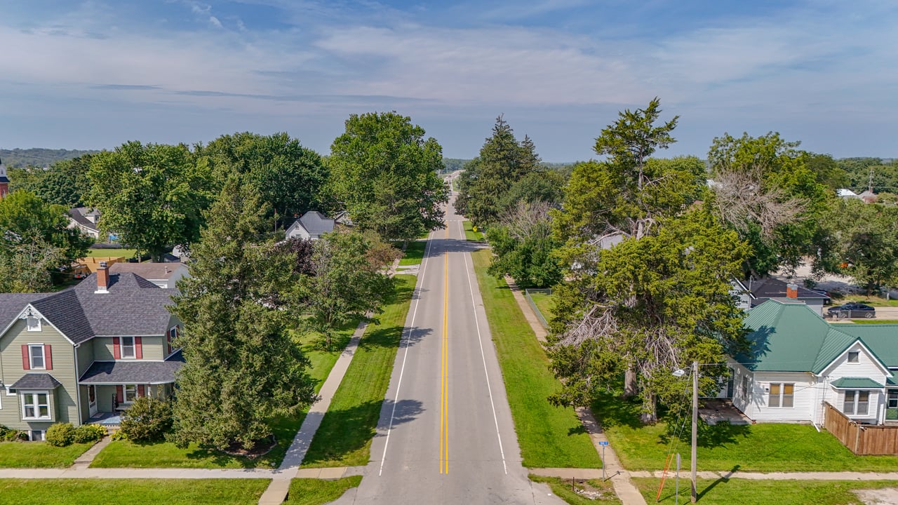 Aerial view of a tree-lined residential street with detached homes and sidewalks.