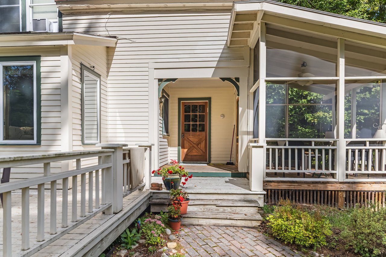 Camp Woodbine’s covered front entry with a wooden door, broad porch, and flower pots by the steps.