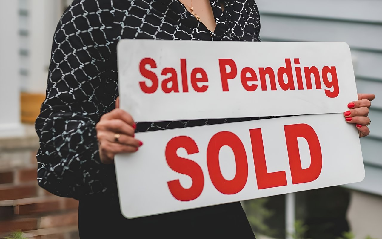 A person holds signs reading “Sale Pending” and “SOLD.”