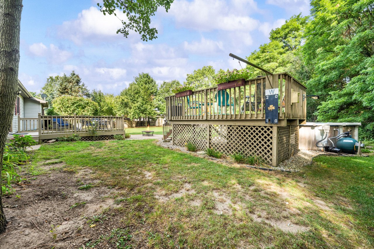 Backyard with a raised wooden deck, lattice skirting, and hot tub among mature trees.