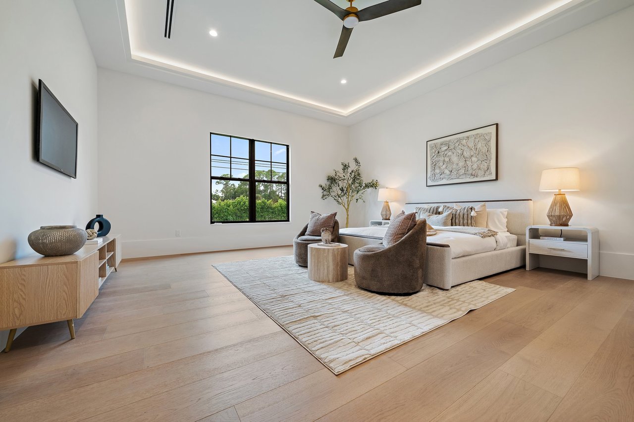 Staged primary bedroom with a king bed, tray ceiling, and large black-framed window.