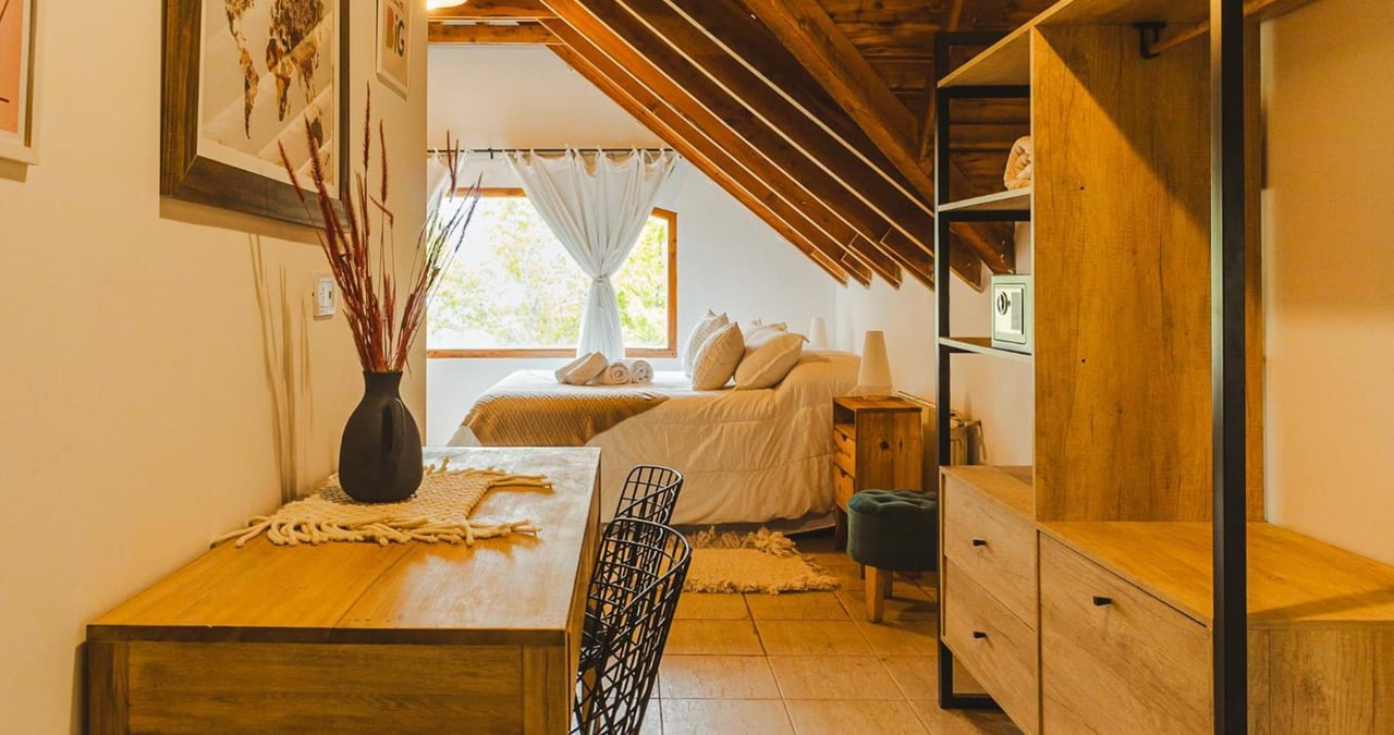 Boutique hotel bedroom with a white bed beneath a timber ceiling and warm wooden furnishings.