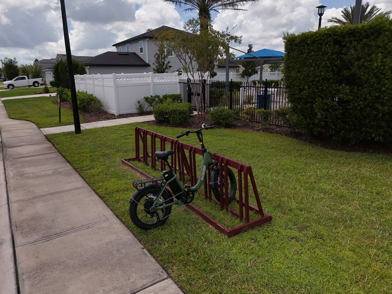 Neighborhood sidewalk with a bicycle at a red rack beside a fenced pool area.
