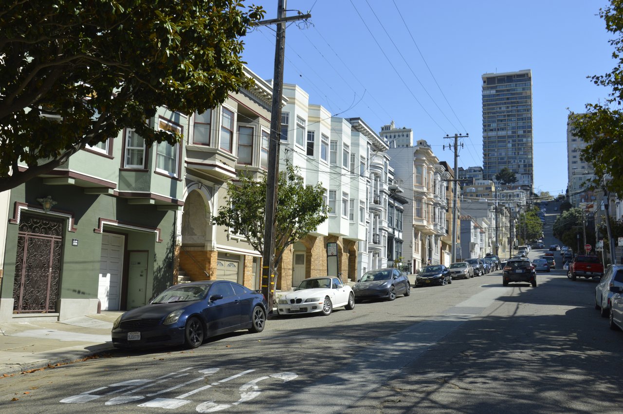 Row of Edwardian-style San Francisco flats with parked cars and the downtown skyline in the distance