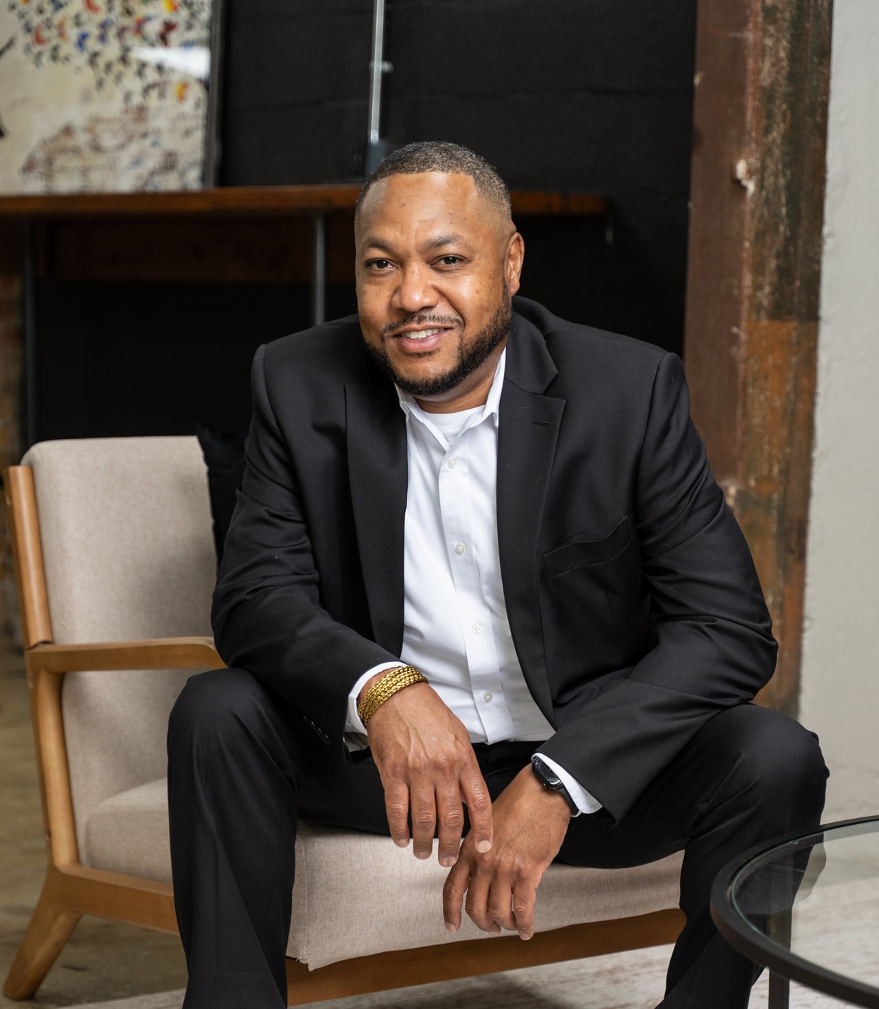 Randy Lane seated in a beige chair, wearing a black suit and white shirt.