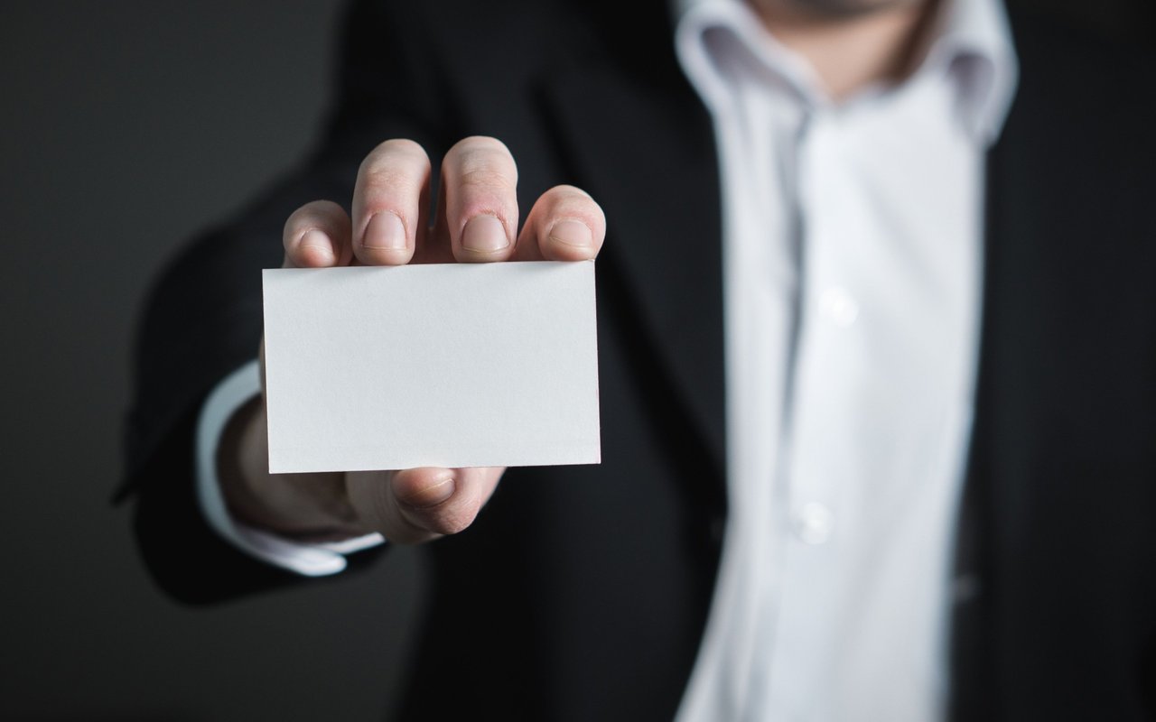 A person in a black suit holds out a blank white card.