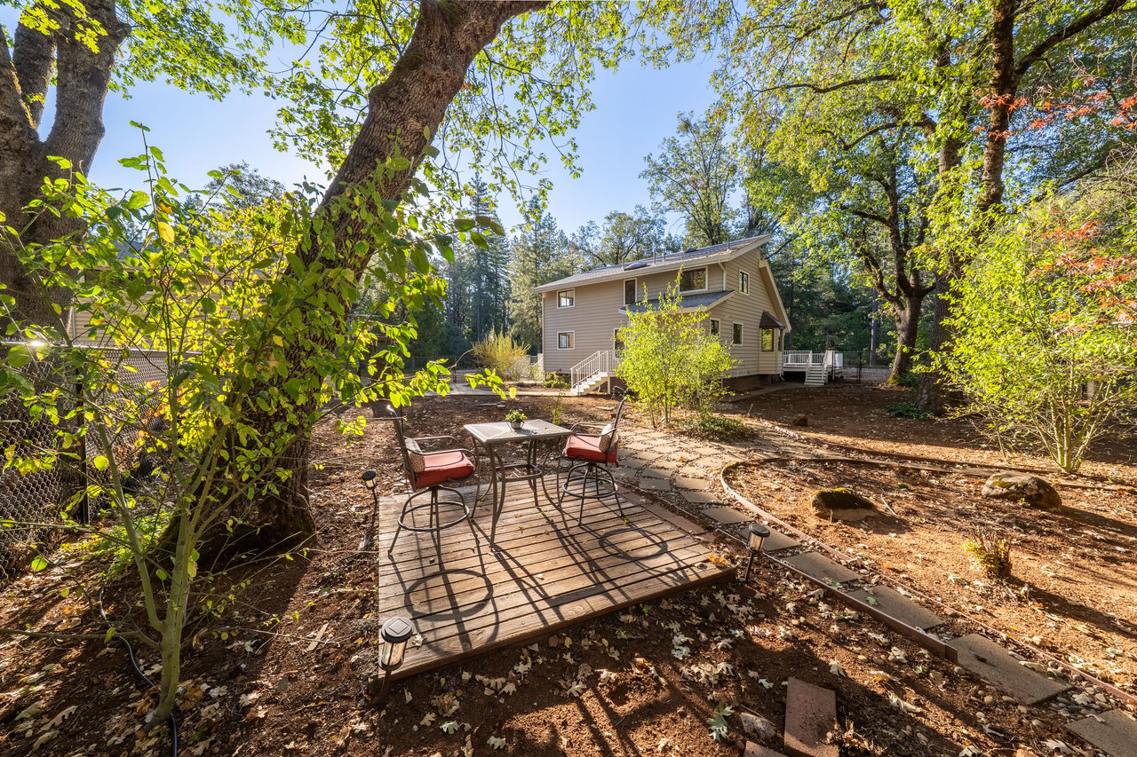Two-story house in a wooded backyard, with a wooden deck and patio table and chairs.