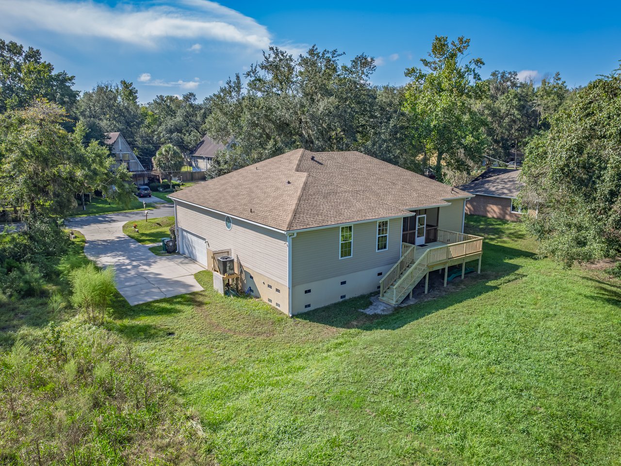 Aerial view of a single-story home with a raised wooden deck and stairs overlooking a grassy yard.
