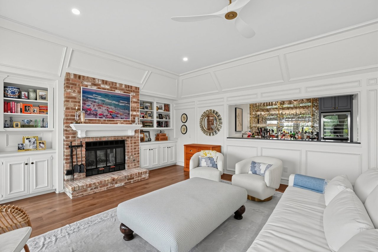 Living room with a brick fireplace, white built-ins, paneled ceiling, and seating beside a built-in bar.