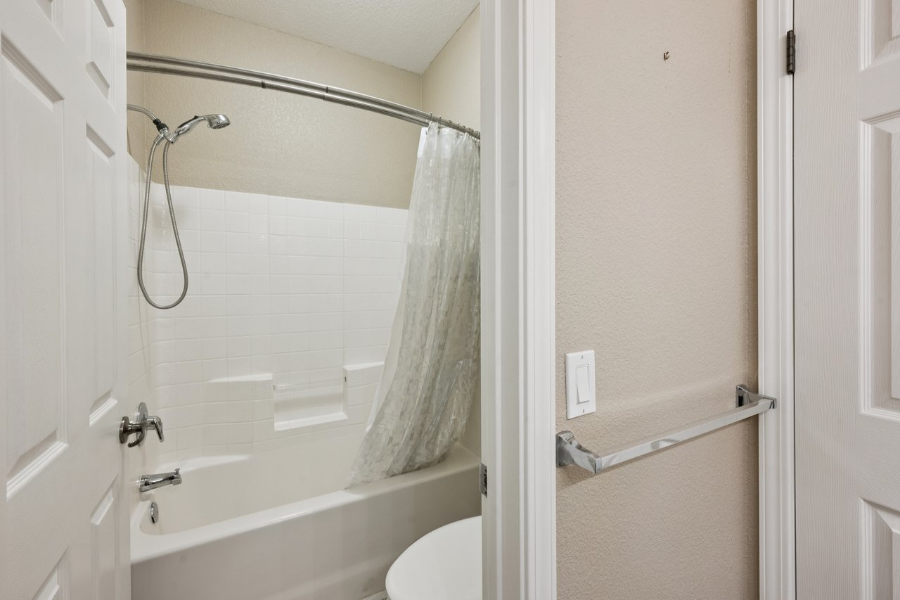Bathroom with a white tub, tiled surround, and handheld showerhead.