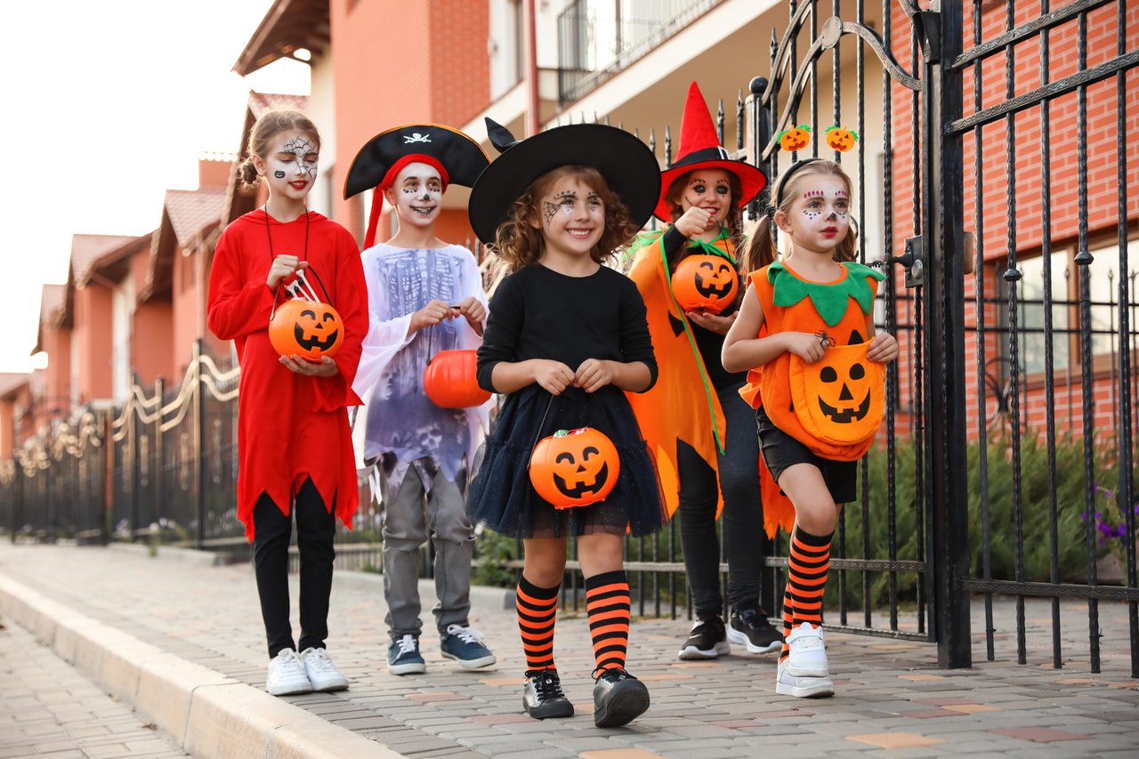 Children trick-or-treating along a decorated Newport Beach street lined with coastal homes at dusk.