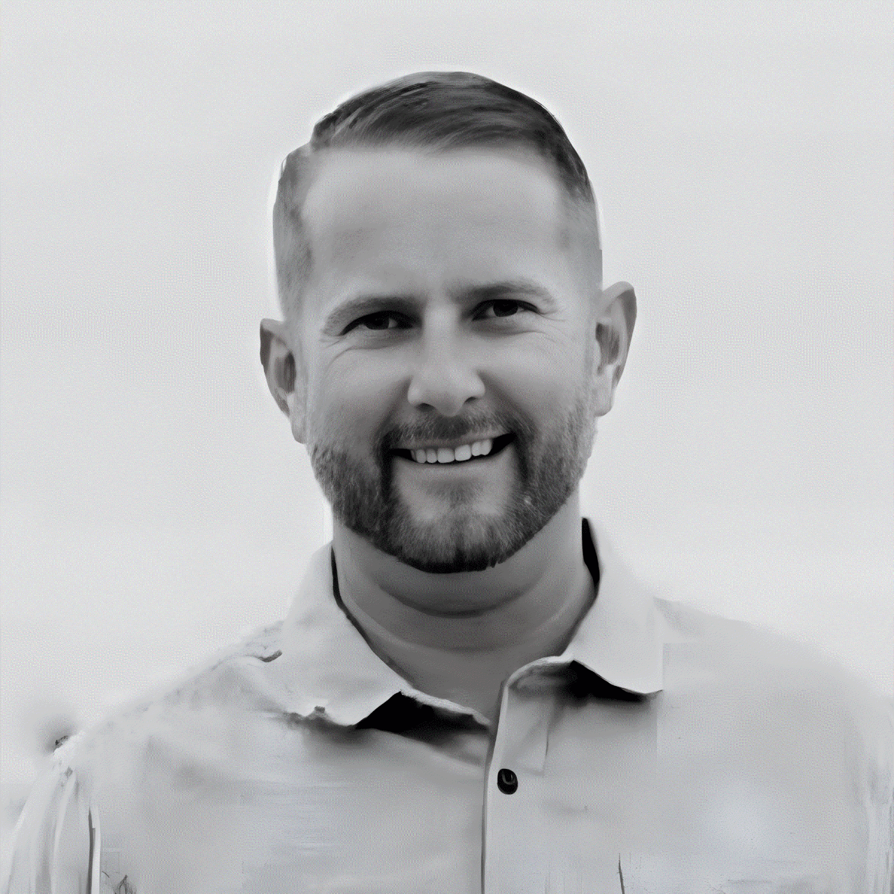 Smiling bearded man in a light collared shirt, photographed in black and white.