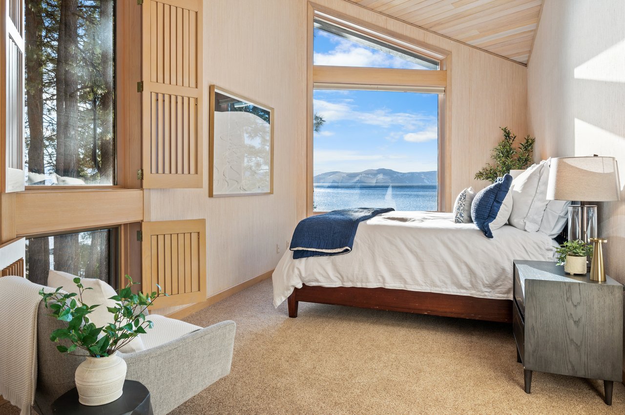 Lakefront bedroom with a large bed and tall windows overlooking the lake and mountains.