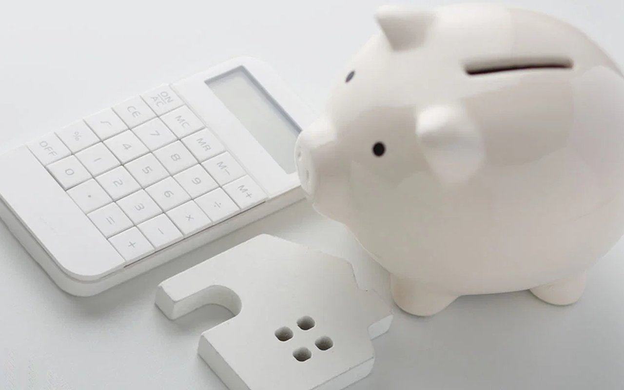 White piggy bank beside a calculator and a small house-shaped object.