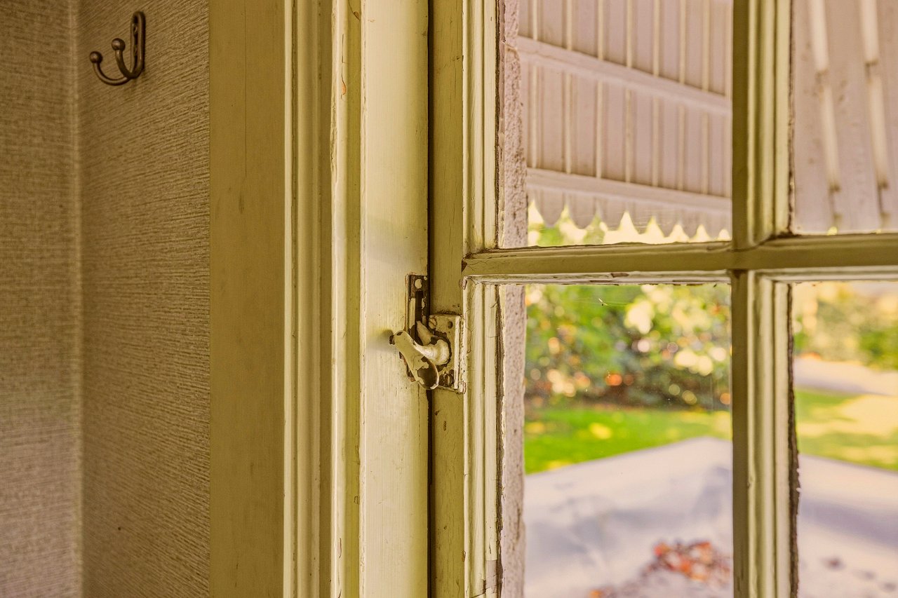 Old painted window with a worn latch, looking out onto a green lawn and walkway.