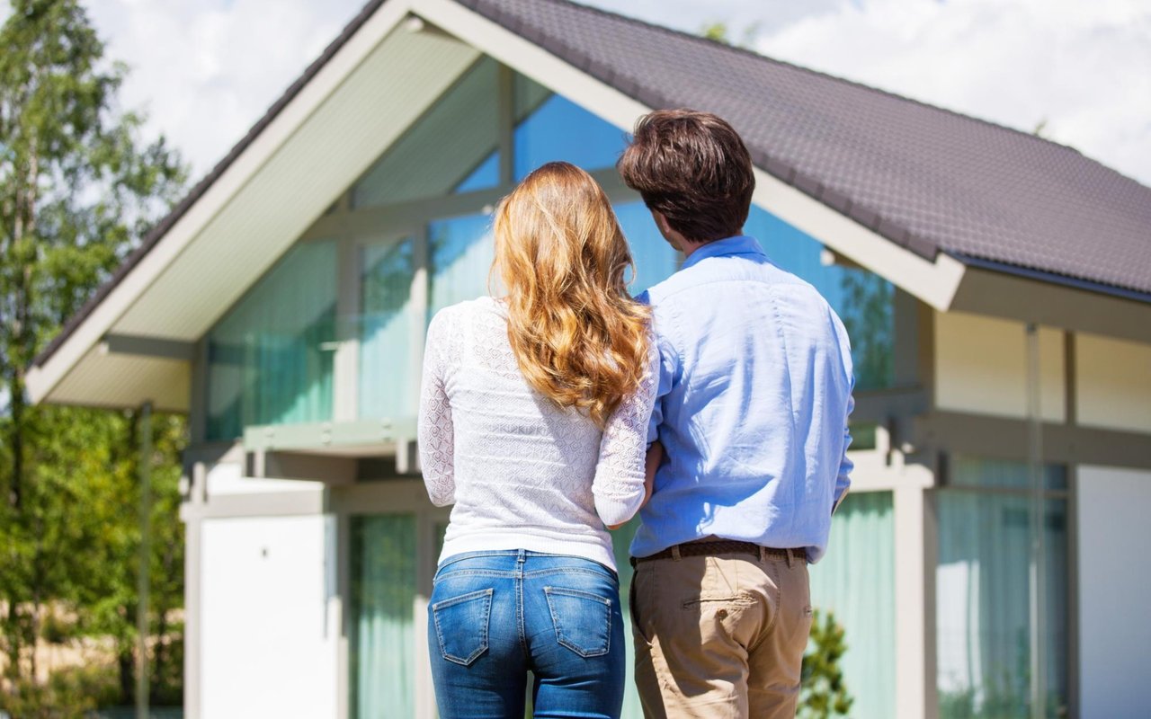 Modern home with a couple looking up at its large glass facade.