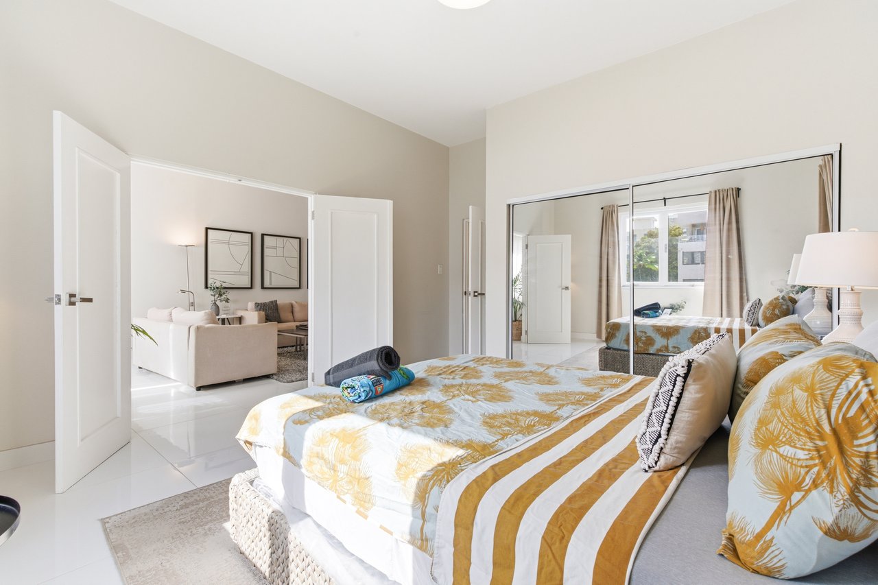 Furnished bedroom with mustard botanical bedding, mirrored closet doors, and a view into the living room.