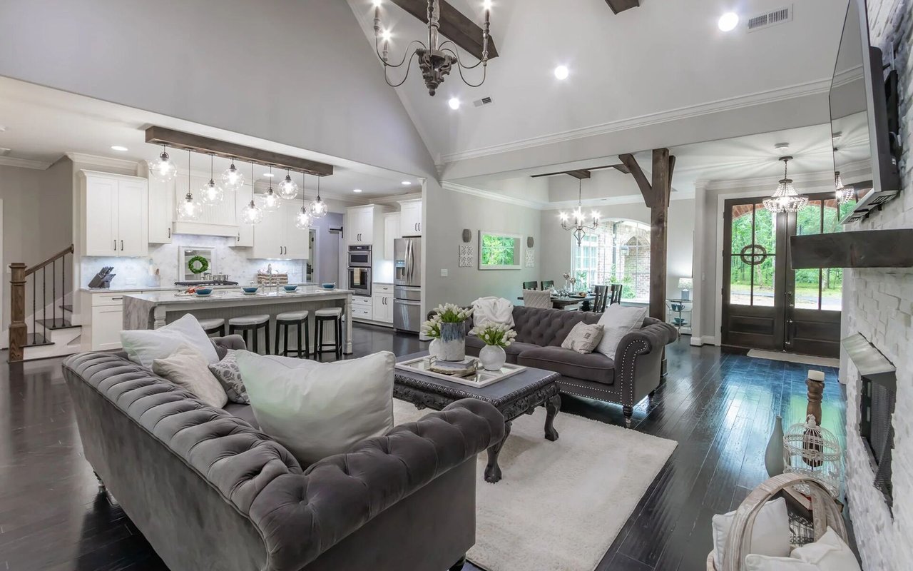 Open-plan living room and kitchen with gray tufted sofas, white cabinetry, and dark wood floors.